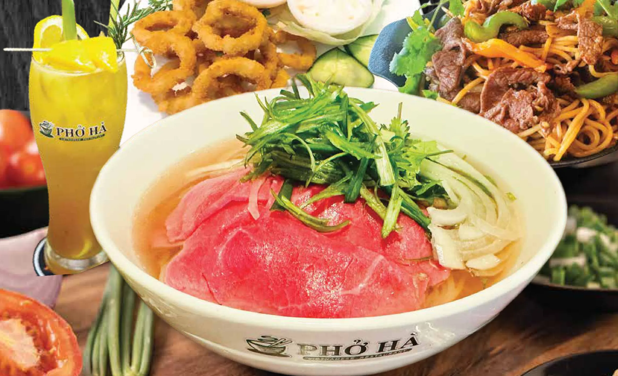 A bowl of Phở Hà's beef pho topped with fresh herbs, served alongside calamari, spring rolls, and stir-fried beef noodles